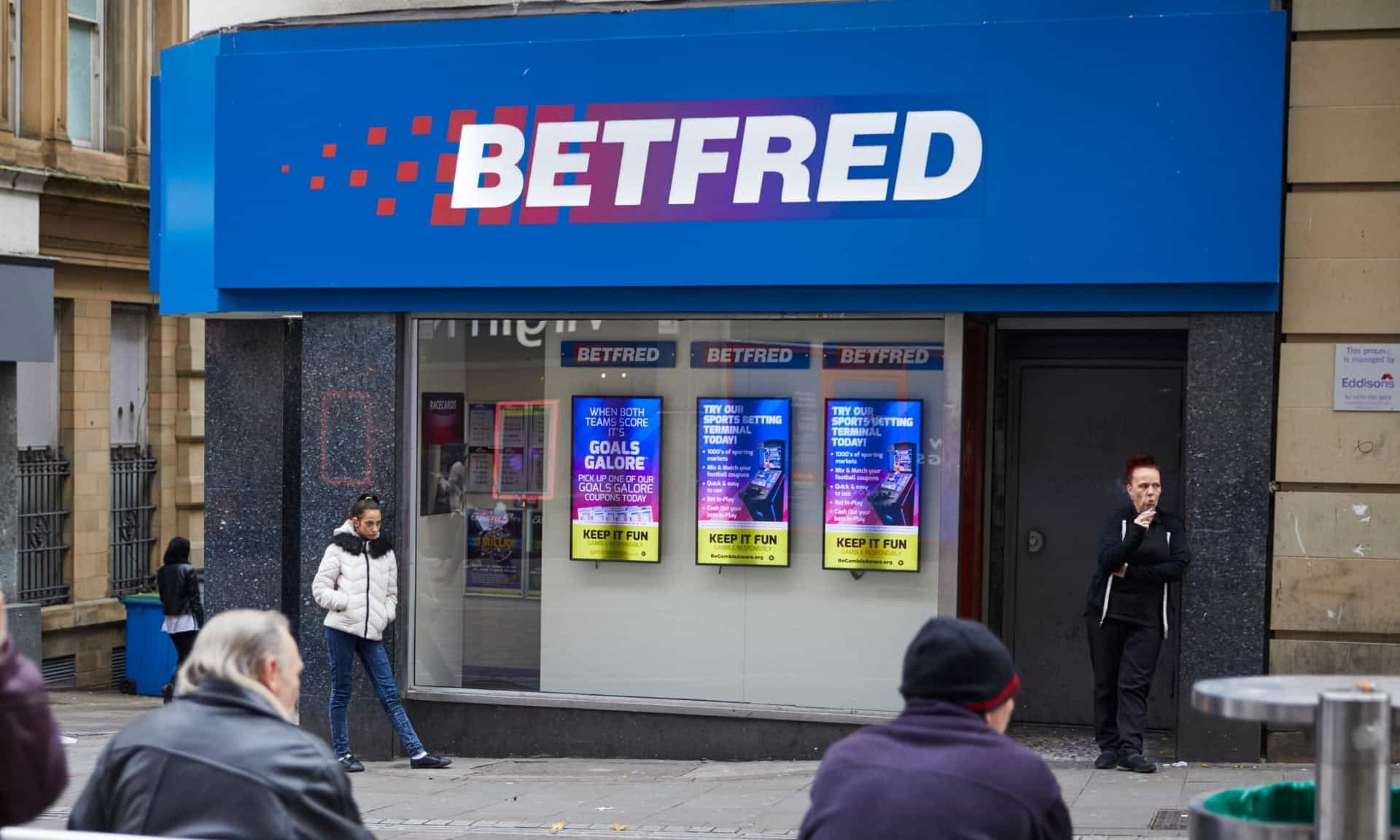 A Betfred shop on the highstreet, with members of the public walking about.