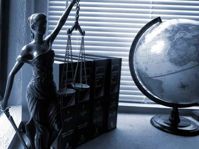 A state of Lady Justice holding the scales of justice standing next to legal books and a globe.