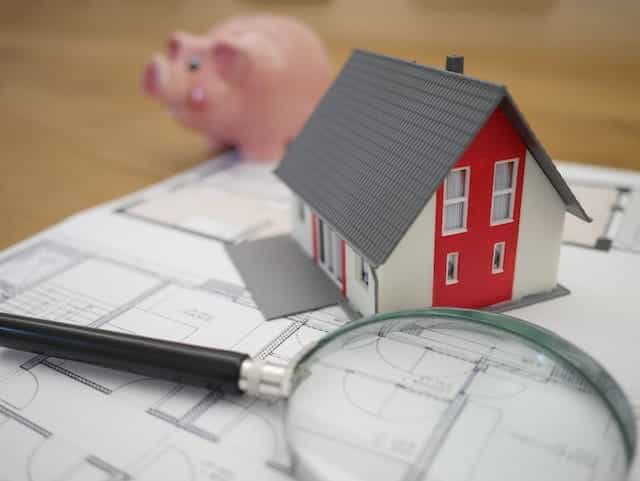 A magnifying glass next to a model of a house and a piggy bank.