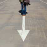 A person standing at the base of a downward pointing arrow painted onto a smooth concrete floor.