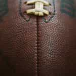 A very close up shot of an American football, featuring its iconic ridge and pigskin brown texture.