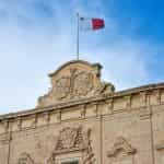 A white and red flag hoisted on a building against a blue sky.