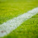 A close up shot of a field or pitch used for playing sports, with a white line prominently spray painted onto the green grass.