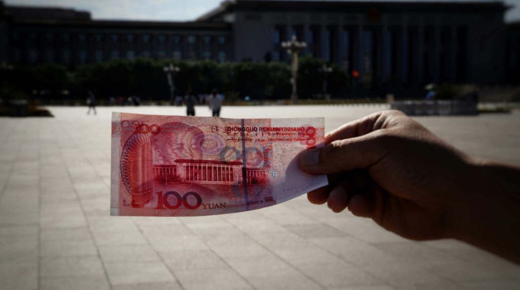 A hand holding a 100-yuan banknote